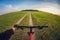 Cyclist on a dirt road in a field for sowing at sunset POV