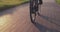 Cyclist is pedaling on cycle path in park at sunset. Gear system of road bicycle. Bike wheel rotation. Woman twists pedals on aero