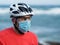 Cyclist sportsman wears protective face mask and white bike helmet on blue ocean.
