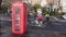 Cyclists in a cycle lane go past a British phone box in the rain