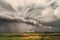 Cyclone storm over fields and meadows approaches the hilly valley. Rainy cloudy day