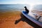 Dachshund sitting on windsurf board at the beach. Cute black doggy is loving surf