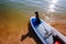 Dachshund sitting on windsurf board at the beach. Cute black doggy is loving surf