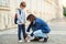 Dad adjusts shoes to son while preparing him to school outdoor. Father and son with backpack walking to school together