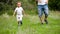 Dad and baby running through the green grass in the park, holding hands, in slow motion.