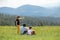 Dad and children are sitting on the top of the mountain. Girl shows a hand into the distance