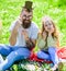 Dad and daughter sits on grass at grassplot, green background. Child and father posing with eyeglases, crown and top hat