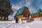 Dad, mom and little girl stand near a snowman next to a wooden cottage