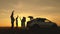 Dad plays and dances happily with his daughters, mom and children have fun at sunset next to the car. parents and