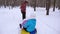 Dad rolls baby and mom on snow saucer running in winter snowy forest and laugh. Man and woman with their daughters had