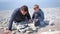 Dad and son are igniting the coals in the bonfire on the handmade stones brazier at sea beach.