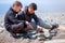 Dad and son are igniting the coals in the bonfire on the handmade stones brazier on sea beach. Family camping.