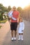 Dad with two young daughters is standing on sidewalk in rays of the setting sun