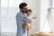 Daddy kisses baby standing near modern crib in cozy nursery