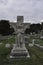 Damaged Angel Statue with One Arm Missing and Spread Wings on a Cross Looking Down in a Cemetery