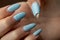 Damaged nail polish of blue color on the regrowth nails of the hand with white skin. Need in correction. Macro close-up