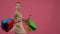 Dancer in costume spinning around with multicolored shopping bags. Pink background. Slow motion