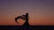 Dancer holds a veil in her hands, she dances a belly dance on the beach. Silhouette