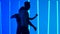 Dancers practice a series of spins against a backdrop of bright blue neon lights in a dark studio. Silhouettes of a