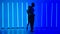 Dancers practice a series of spins against a backdrop of bright blue neon lights in a dark studio. Silhouettes of a