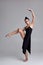 Dancing ballerina in a black dress. Contemporary graceful performance on a gray background.