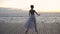 Dancing ballerina in white ballet tutu and pointe on embankment above ocean or sea at sunrise or sunset. Young