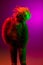 Dancing. Energy. Expressive young woman in fur coat posing over magenta studio background in green neon light. Concept