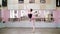 in dancing hall, Young ballerina in black leotard performs 1 arabesque, raises her leg up behind elegantly, standing