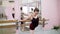 In dancing hall, Young ballerina in black leotard stretching backward at barre, elegantly, standing near barre at mirror