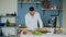 Dancing young man cooking vegetarian breakfast cutting vegetables for salad in kitchen at home