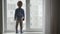 Dangerous situation with child at home, little boy stands on windowsill and looking out the window with toy car in hand