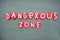 Dangerous zone, creative sign composed with red colored stone letters over green sand