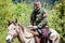 Danisparauli, Georgia - May 8, 2017. Georgian man in  camouflage jacket riding a horse on dirt road in mountains