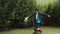 Dapper man riding a unicycle while juggling with his hat in his backyard