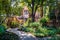 Dappled sun on a curving path with lush tropical plants everywhere and a brick building in the background