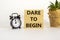 Dare to begin symbol. Wooden blocks with words `Dare to begin`. Beautiful white background, black alarm clock, house plant.