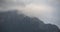 Dark atmospheric surreal landscape with a dark rocky mountain peak in low clouds in a gray cloudy sky