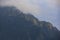 Dark atmospheric surreal landscape with a dark rocky mountain peak in low clouds in a gray cloudy sky