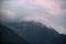 Dark atmospheric surreal landscape with a dark rocky mountain peak in low clouds in a gray cloudy sky