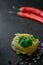 On a dark background raw fettuccine pasta with cilantro leaves, coarse sea salt black and red peppercorns and chili