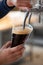 Dark beer in plastic cup flowing from beer tap with nice foam close-up in female bartender hands