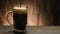 Dark beer pouring in glass on wooden background