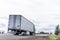 Dark big rig diesel semi truck transporting commercial cargo in dry van semi trailer moving on the flat road