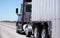 Dark big rig semi truck with bulk corrugated trailer transports