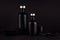 Dark black minimalist interior. Blank black cosmetics bottles on dark wood board with copy space.