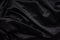 Dark black silky, satin fabric, wave, draperies. Beautiful textile backdrop. Close-up. Top view