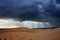 Dark black storm clouds with piercing sunrays covering desert landscape.