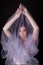 dark blond girl in a black dress wrapped in a lilac veil stands with her hands closed up