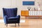 Dark blue armchair with a vintage cabinet in the background in a living room interior