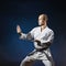 On a dark blue background, an athlete with a black belt performs formal karate exercises